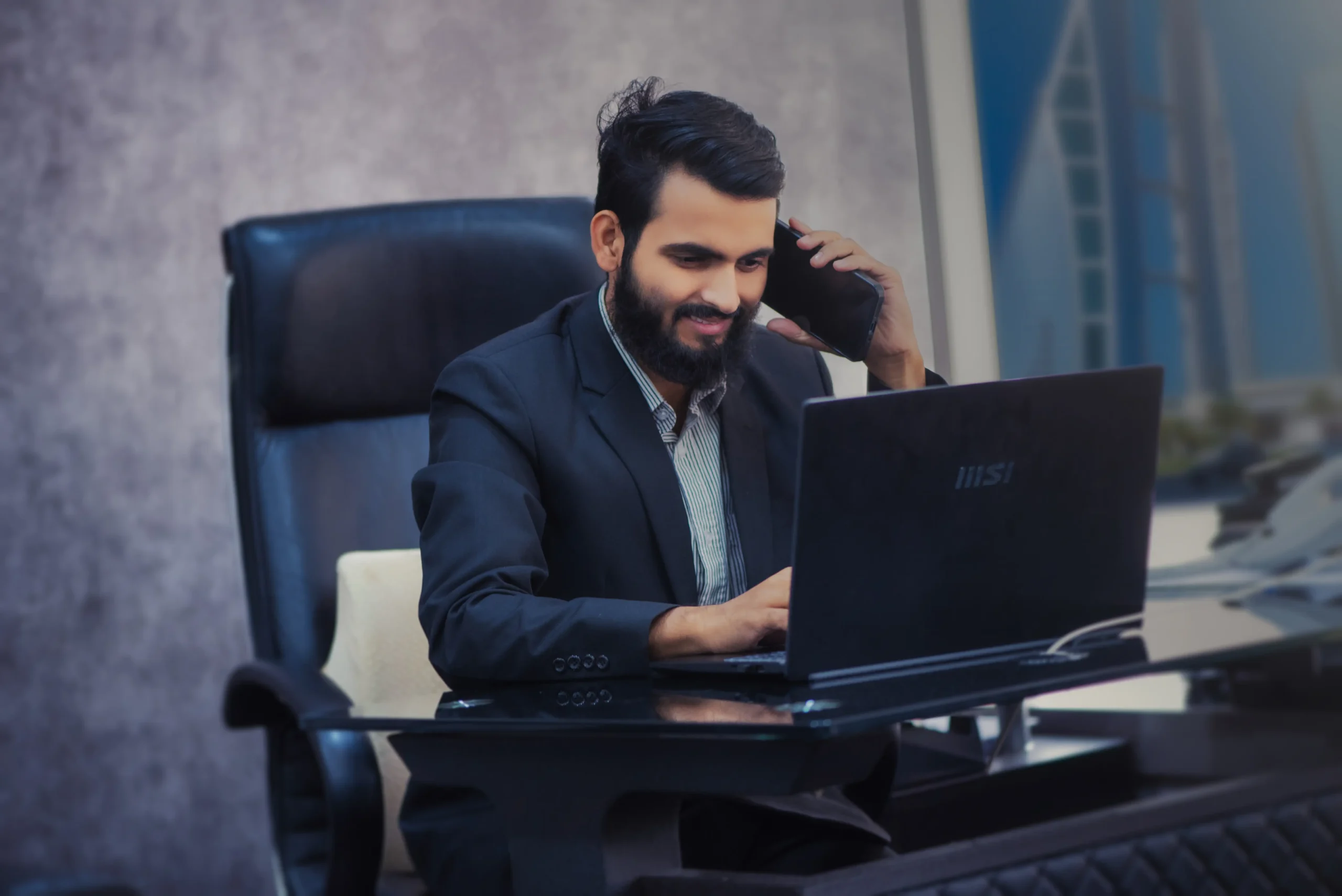 A man in a suit seated at his desk, engrossed in a phone call, embodying professionalism and accessibility for reaching out to the blog.